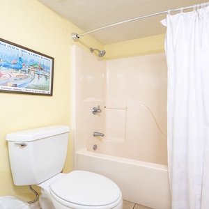 Guest bathroom featuring a tub/shower combo, a white toilet, and a colorful art piece on the wall for a cheerful touch