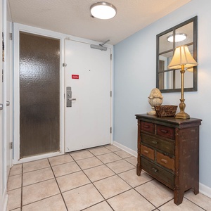 The entryway features a charming wooden dresser, a decorative lamp, and a large mirror against soft blue walls