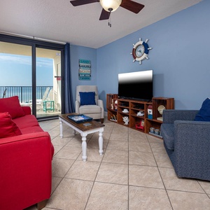 Living room with red sofas and queen sleeper, a large TV, and a balcony offering a beautiful coastal view