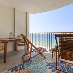 Enjoy a relaxing view from this balcony with wooden seating, colorful cushions, and a vibrant area rug overlooking the beach