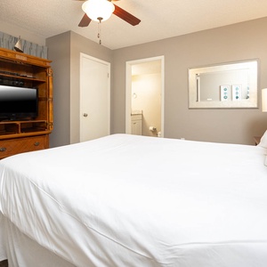 A cozy guest bedroom features a plush queen bed, wooden entertainment unit with TV, and access to a bathroom