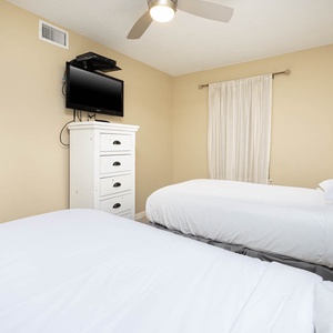Guest room featuring two comfortable twin beds, a wall-mounted TV, and a charming white dresser against a warm beige backdrop