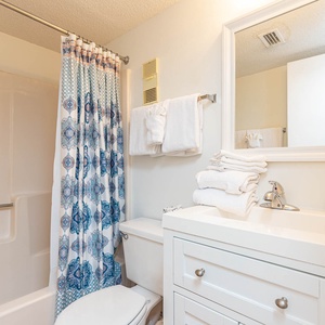 This bathroom features a clean design with a white vanity, plush towels, and a colorful shower curtain for a refreshing touch