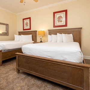 This guest bedroom features two comfortable queen beds, wood accents, and vibrant coral-themed artwork for a relaxing stay
