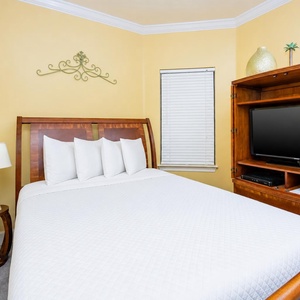 Unwind in this cheerful guest bedroom featuring a queen bed, a TV for entertainment, and warm yellow walls