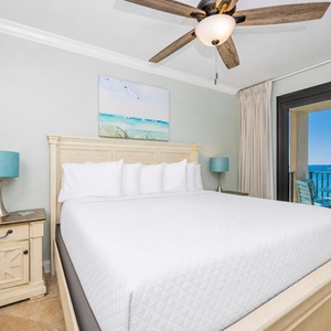 Relax in the serene master bedroom with a large king bed, coastal artwork, and a view of the inviting balcony