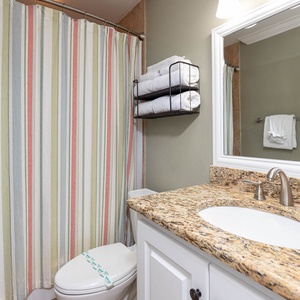 Brightly colored striped shower curtain complements the granite countertop and fresh towels in this inviting guest bathroom