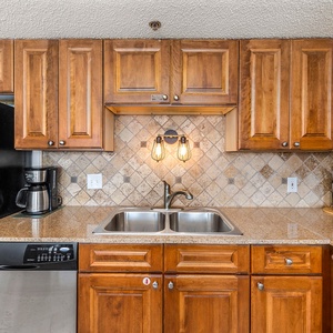 The fully-equipped kitchen features rich wood cabinetry, a coffee maker, and a sleek granite countertop with a double sink