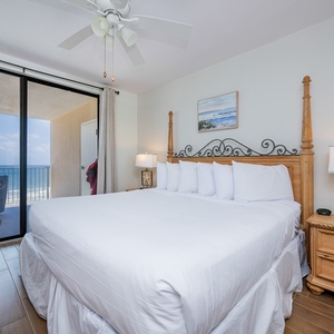The master bedroom features a king bed with white linens and a stunning beachfront view from the sliding glass doors
