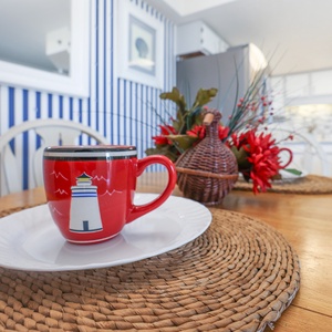 A colorful lighthouse mug sits on a white plate atop a woven placemat, complemented by vibrant floral decor