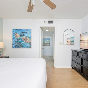 Unwind in the inviting guest bedroom featuring a queen bed, coastal artwork, and a TV