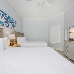 Bright and airy guest bedroom featuring two cozy queen beds, a large TV, and beach-themed decor for a relaxing getaway