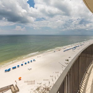 Breathe in the beach air from your balcony, featuring lounge chairs and views of the beach and blue umbrellas