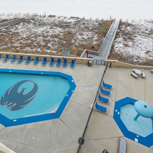 The pool area featuring the Phoenix logo, surrounded by lounge chairs and a shaded seating area, leading to the beach