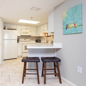 Bright kitchen features white cabinetry, a breakfast bar with seating, and colorful artwork enhancing the space