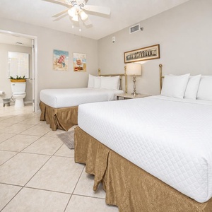 Guest room featuring two double beds with plush white bedding, a bedside lamp, and coastal-themed artwork on the walls
