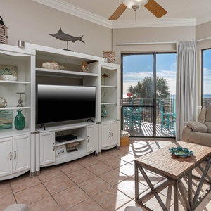Cozy seating area features a TV and a view of the balcony with turquoise chairs overlooking the beach