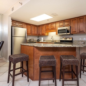The modern kitchen features rich wooden cabinetry, a granite countertop, and a breakfast bar with stylish seating