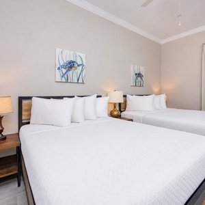 Unwind in this guest room featuring two queen beds, stylish lamps, and coastal turtle artwork for a relaxing stay