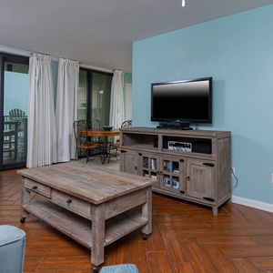 The living area features a cozy blue couch with queen sleeper, a wooden coffee table, and a TV, with a lovely beach view