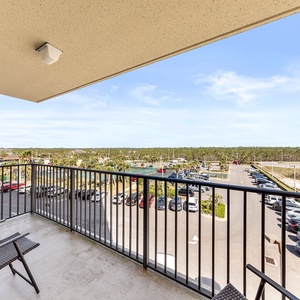 A private balcony features seating and offers a view of lush greenery and a nearby parking area