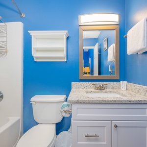 The master bath features a vibrant blue wall, nautical-themed shower curtain, and a sleek vanity for a refreshing experience
