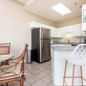 Kitchen area features sleek stainless appliances, bar seating, sleek white cabinetry, and a cozy dining table