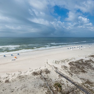 Enjoy the expansive view of the beach, dotted with colorful umbrellas and gentle waves lapping at the beach