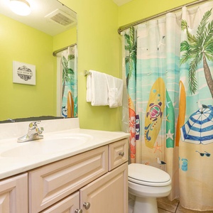 Refresh in this vibrant guest bathroom featuring a spacious vanity, playful surf shower curtain, and bright green walls