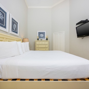 This cozy bedroom features a plush king bed, a mounted TV, and charming coral-themed artwork for a relaxing stay