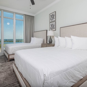 Unwind in a queen bed beneath a bedside lamp while floor-to-ceiling windows frame the gulf and shoreline