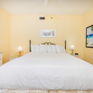 Serene guest bedroom features a large king bed with crisp white linens, soft lighting, and beach artwork on warm yellow walls