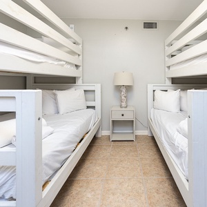 Brightly lit guest room featuring two sets of white twin over double bunk beds and a bedside lamp, perfect for younger guests
