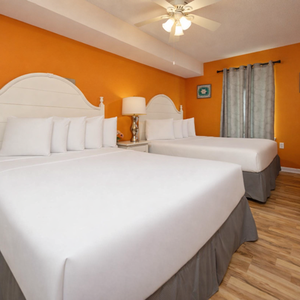 Bright orange walls complement two queen beds in this cheerful guest room, featuring a TV and stylish wooden flooring