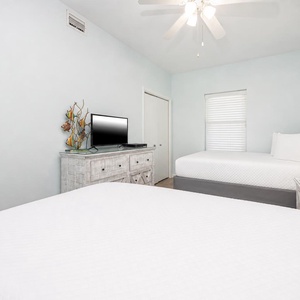 Bright guest bedroom featuring two queen beds, a TV on a rustic dresser, and soft blue walls for a tranquil atmosphere