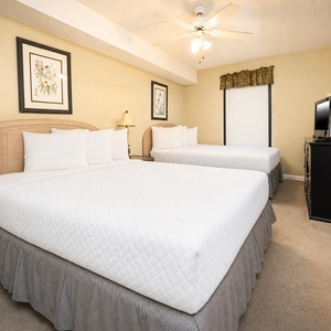 Bright guest room featuring two queen beds, a TV, and framed artwork, creating a welcoming atmosphere for relaxation