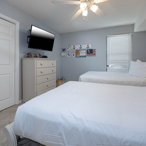 This bright guest bedroom features two full beds, a wall-mounted TV, and charming coastal decor