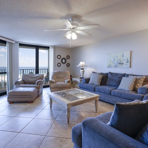 Spacious living area features a blue sofa with queen sleeper, accent chairs, and a stunning gulf view through large windows