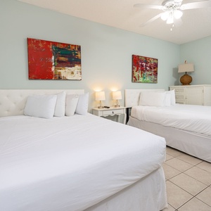 Relax in this inviting guest room featuring two double beds, soft lighting, and colorful artwork on the walls