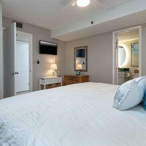 This cozy master bedroom features a comfortable king bed, a mounted TV, and a stylish lamp, with an adjoining bathroom
