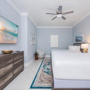 Relax in this guest bedroom featuring two queen beds, a large TV, and coastal artwork for a serene vibe