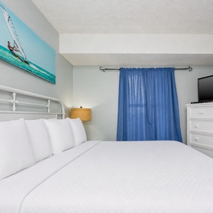 The master bedroom features a comfortable bed, a TV for entertainment, and a serene beach-themed artwork above