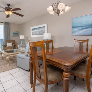 Bright living area features a cozy seating arrangement, dining table, and large windows showcasing a beautiful beach view