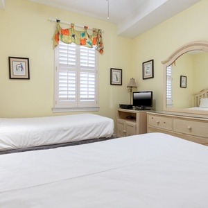 This cozy bedroom features two beds, cheerful yellow walls, a TV, and charming decor, perfect for a restful stay
