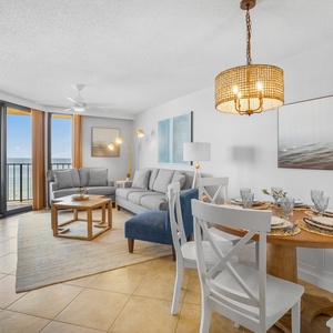 The inviting living area features a cozy gray sofa, a stylish dining table, and large windows showcasing a beachfront view
