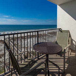 Enjoy a relaxing view from the balcony with a table and chairs overlooking the beach and sparkling waters