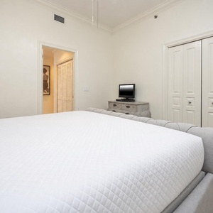 Cozy guest bedroom featuring a queen bed, TV on a dresser, and a warm, inviting atmosphere with neutral tones