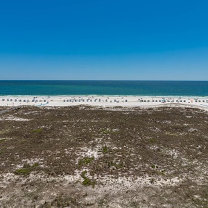 Expansive view of the beach with white sand and turquoise waters, dotted with umbrellas and lounge chairs under a clear sky