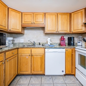 Kitchen featuring warm wood cabinetry, a white dishwasher, and a range of appliances including a Keurig and coffee maker