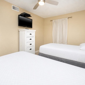Guest room featuring two comfortable twin beds, a wall-mounted TV, and a charming white dresser against a warm beige backdrop